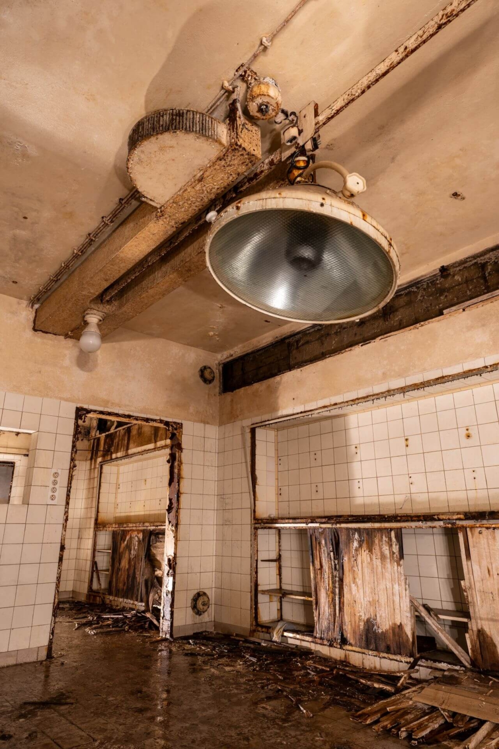 Zeigt einen Operationsraum mit OP-Lampe und vermoderten Regalen im Hintergrund.