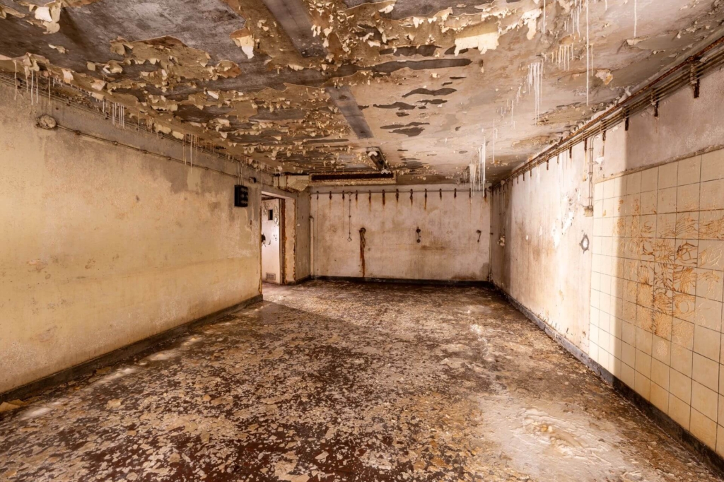 Großes Patientenzimmer, in dem die Farbe von der Decke blättert.