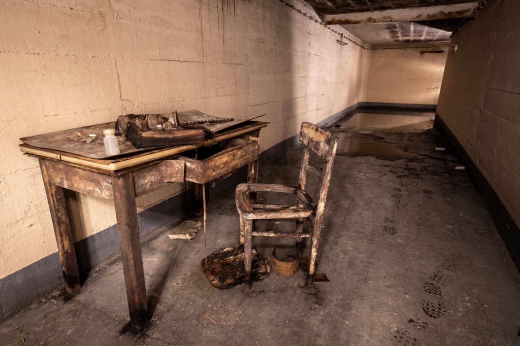 Vermoderter Schreibtisch mit Stuhl davor steht in einem Zugangsflur.