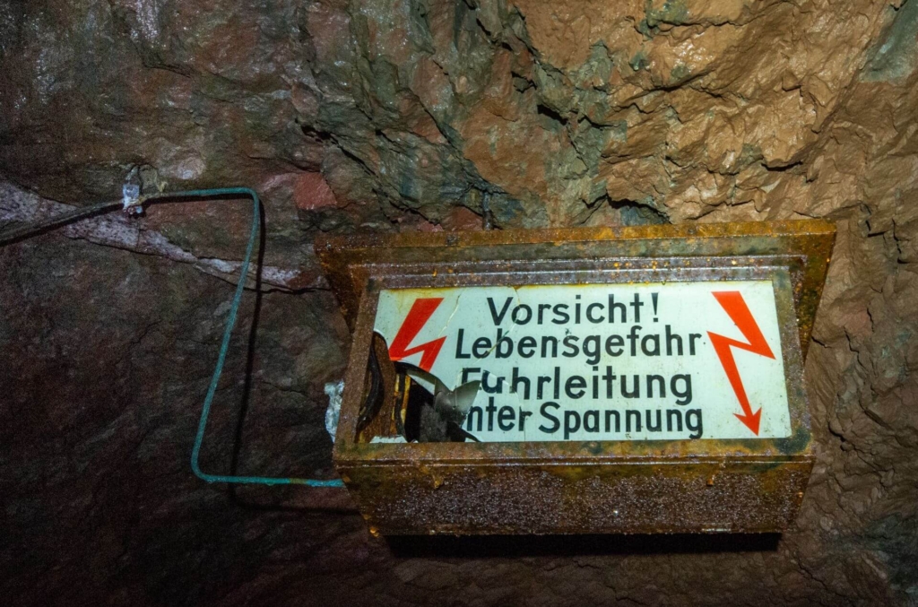 002_fahrleitung Zeigt ein beleuchtetes Warnschild mit der Aufschrift "Vorsicht! Lebensgefahr Fahrleitung unter Spannung". links und rechts sind rote Blitze aufgemalt.