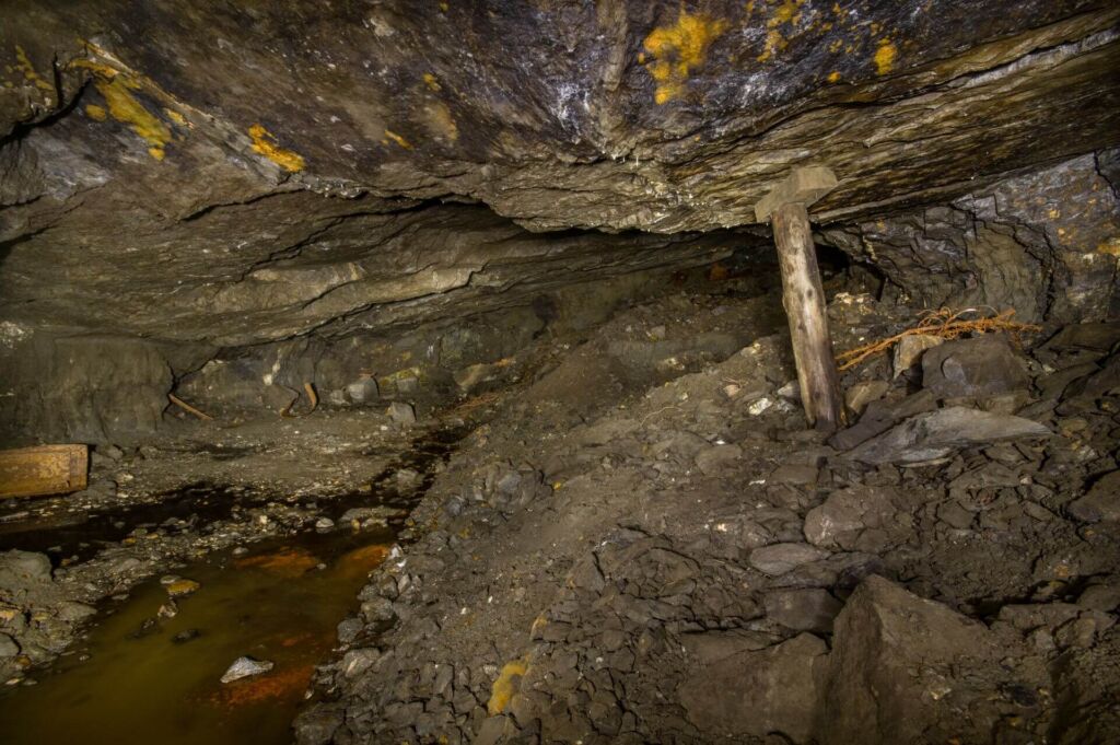 007-altbergbau-abbau Zeigt einen Holzstempel, der im Pfeilerkammerbau steht und die Firste stützt.