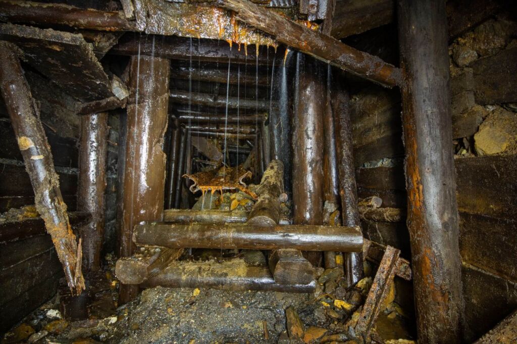018-altbergbau-eisenerzgrube-ruettelblech Zeigt ein rostiges Rüttelblech im Holzausbau. Von oben tropft Wasser runter.