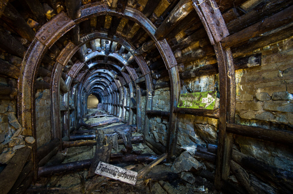 033_fahrung_gesperrt Zeigt einen schmalen Stollen mit Stahlausbau im gelben und blauen Licht.