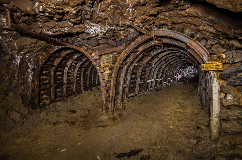 037_die zwei_wege_seitlich Zeigt einen Streckenabzweig in Stahlsegmentausbau. Rechts hängen zwei Holzschilder. "Fahrung zur 150 m Sohle" und "Querschlag 102"