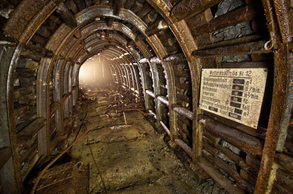 040_wettermessstelle_gl Zeigt einen Stollen im Stahlsegmentausbau und massiven Holzverzug. An der Seite hängt ein Bild mit der Aufschrift "Wettermeßstelle Nr. 12"