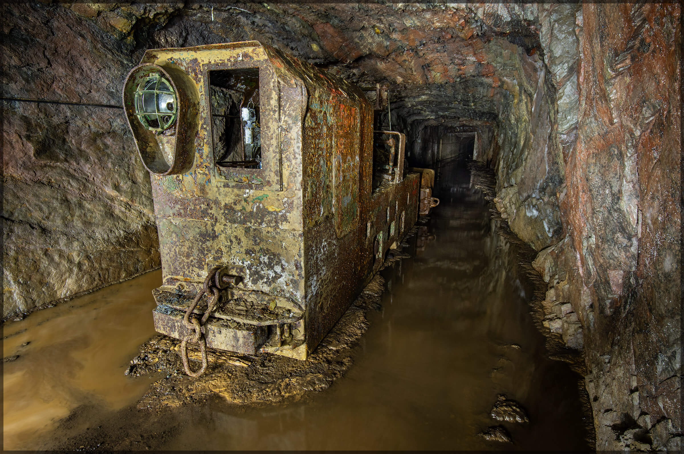 In der stillgelegten Grube Amalienhöhe steht eine verrostete Lore auf einem überschwemmten Schienenweg.