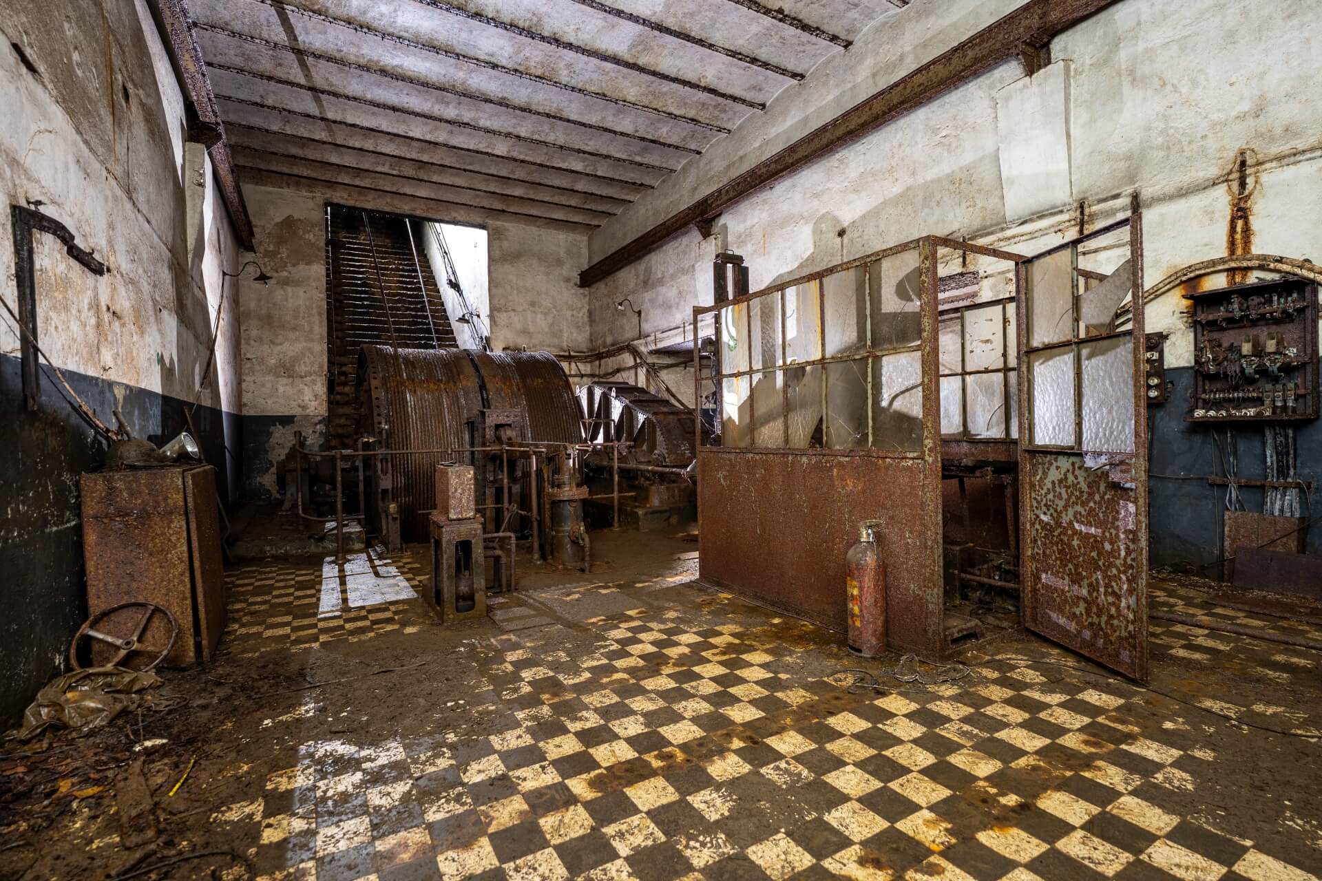 Eine verlassene Halle im Bergwerk zeigt rostige Maschinen und einen gefliesten Boden.